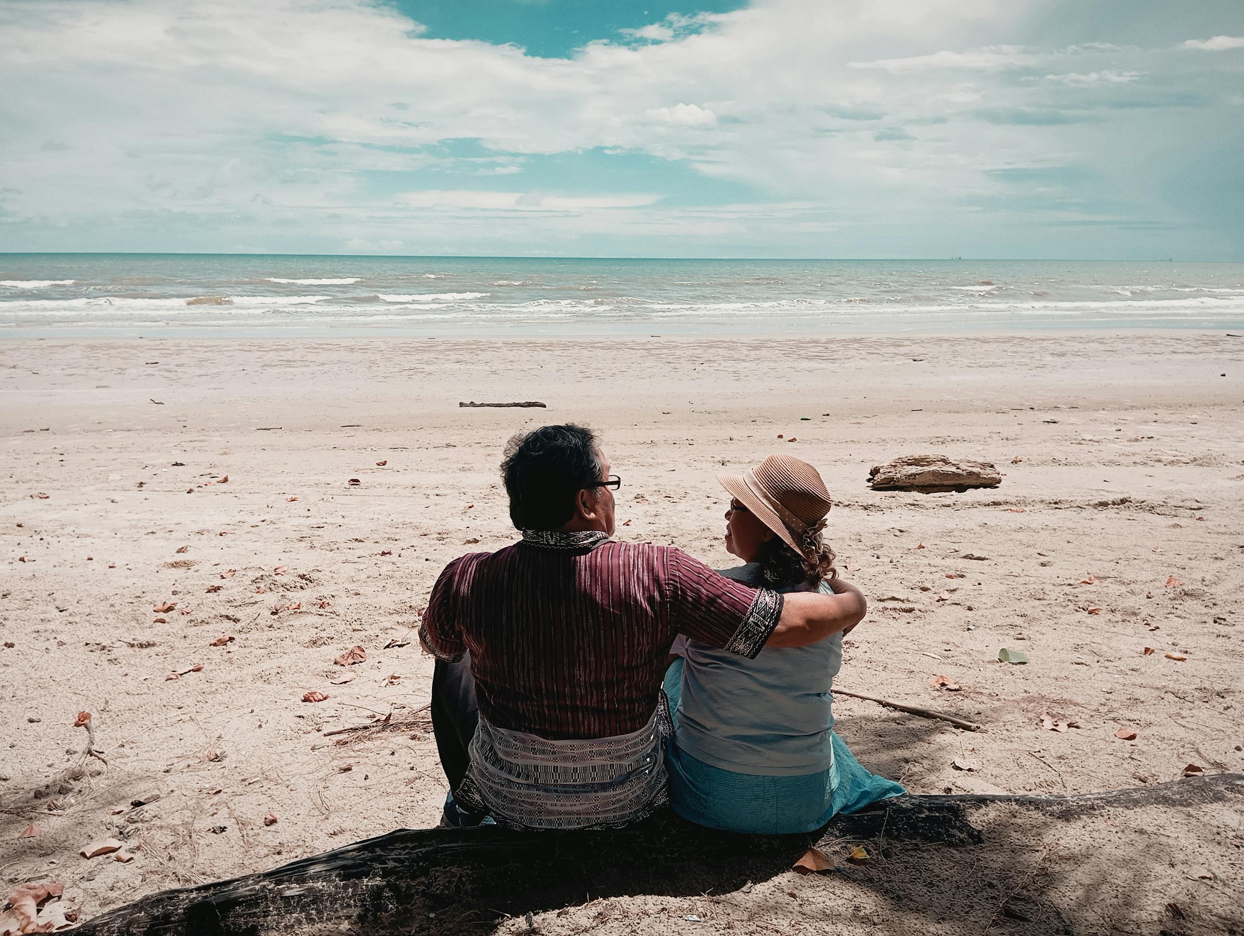 A couple sitting on the beach, enjoying the serene ocean view together.
