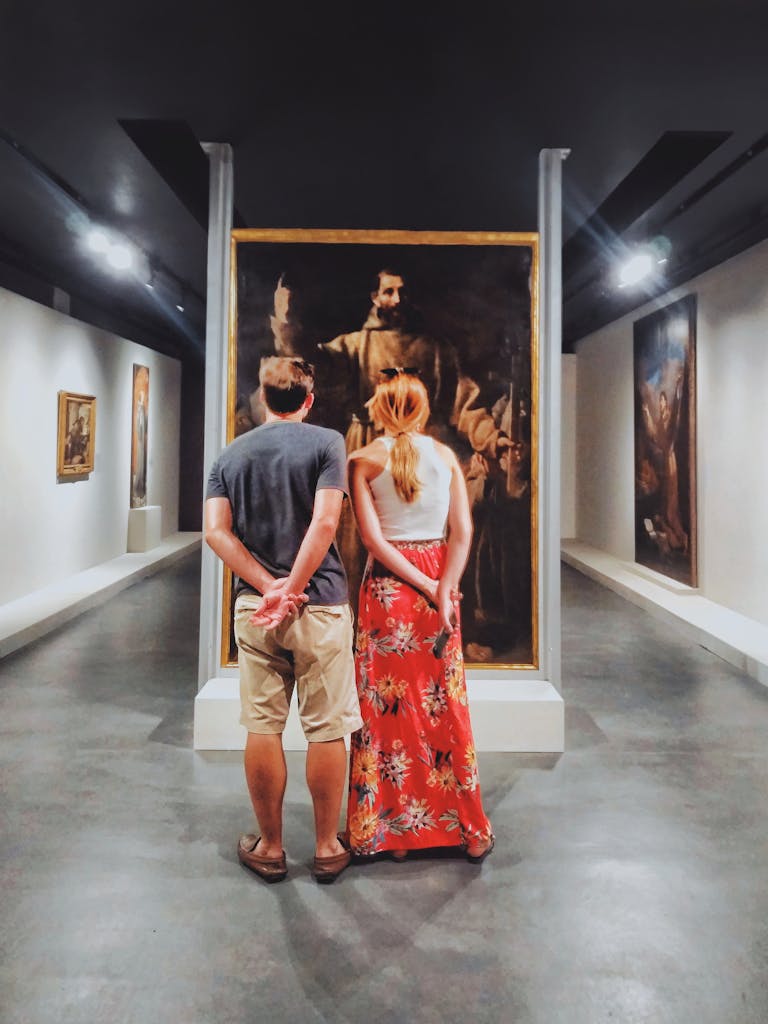 A couple stands inside an art gallery in Brazil, engaging with classical paintings.