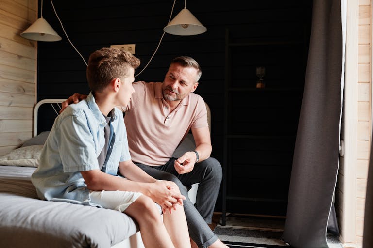 A father bonding with his teenage son in a cozy bedroom, sharing advice and conversation.