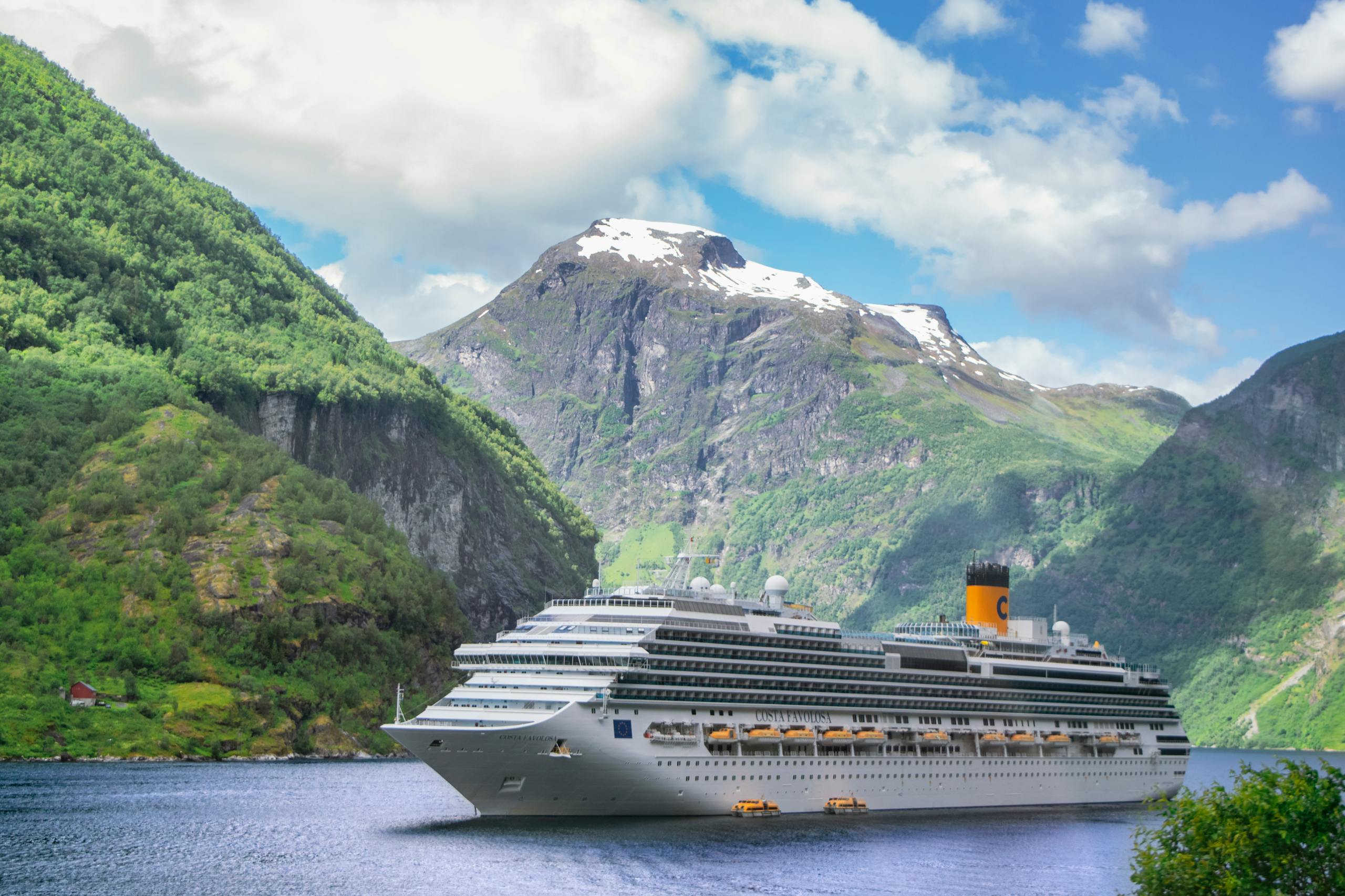 A grand cruise ship navigates the serene Geiranger Fjord in Norway, surrounded by majestic mountains.