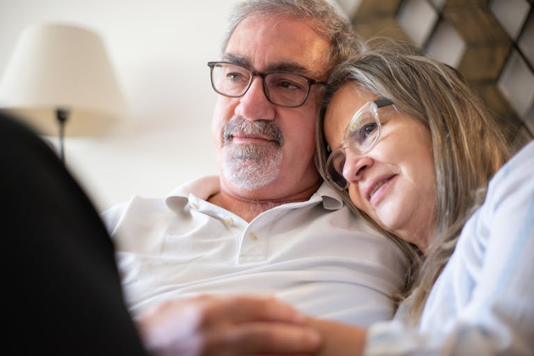 A loving elderly couple embracing and smiling indoors, conveying warmth and happiness.