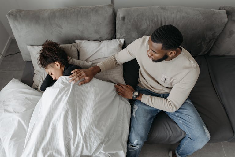 A man tenderly cares for a woman resting on a couch, illustrating compassion and support.