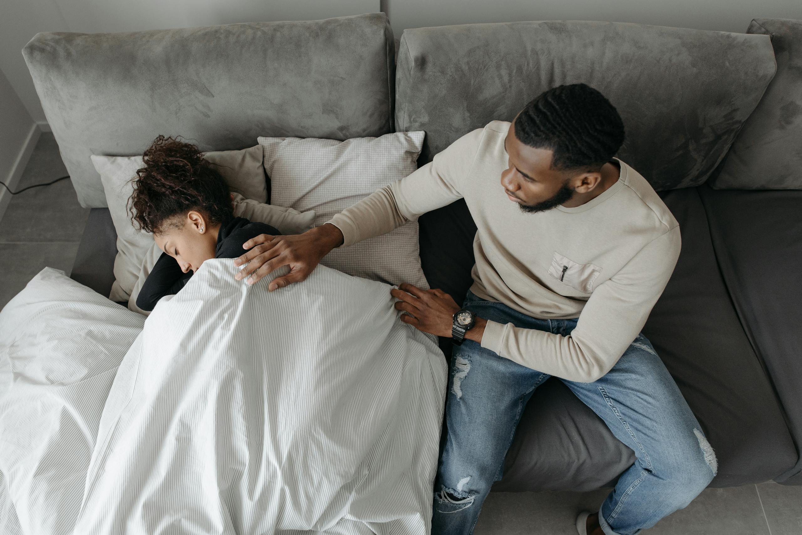 A man tenderly cares for a woman resting on a couch, illustrating compassion and support.