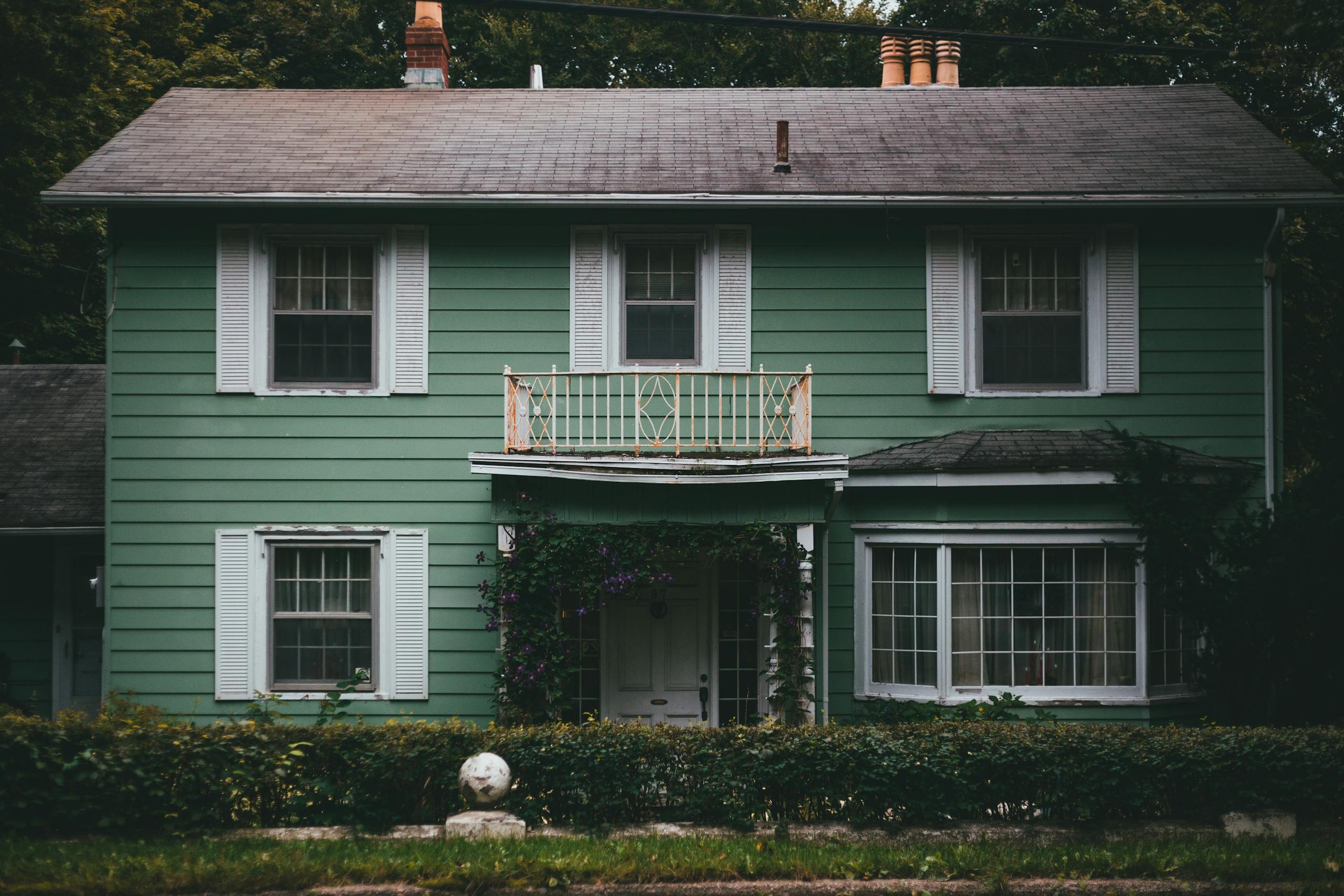 A picturesque green wooden house with a charming facade and lush surroundings, perfect for a peaceful home setting.