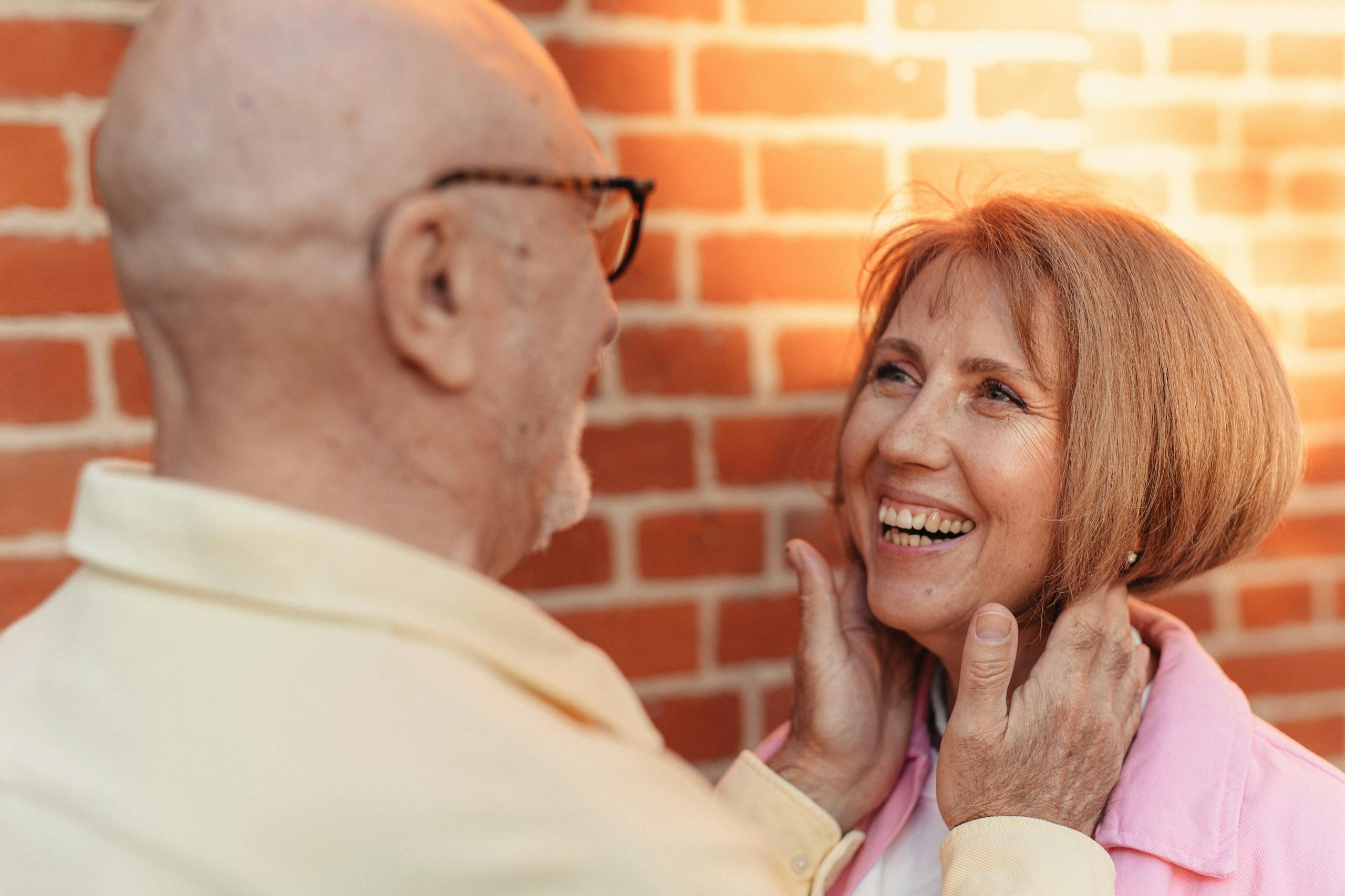 A senior couple embraces lovingly against a brick wall, epitomizing affection and happiness.