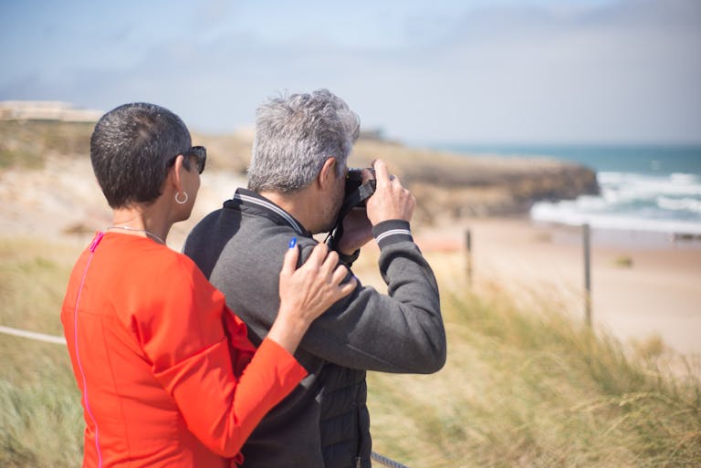 A senior couple enjoying photography at a scenic Portuguese beach.
