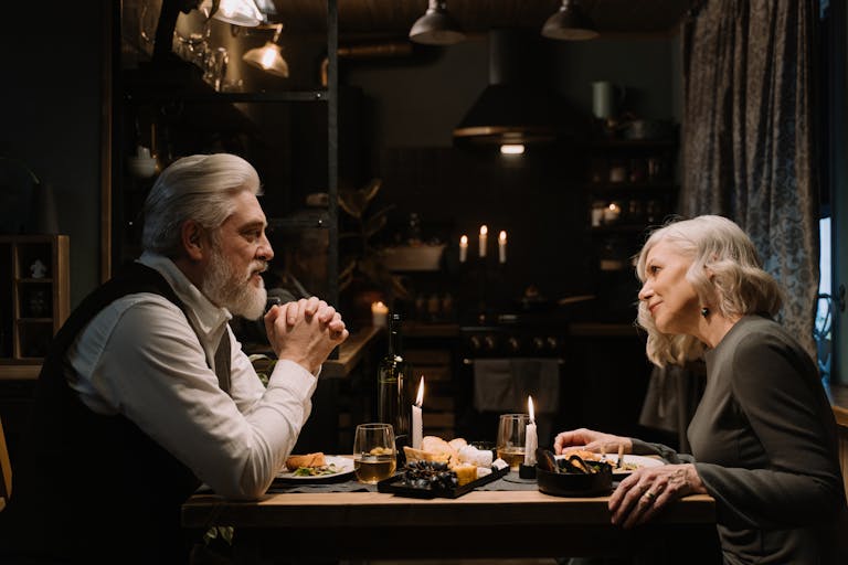 A senior couple shares a romantic dinner by candlelight in a cozy home setting, expressing love and companionship.
