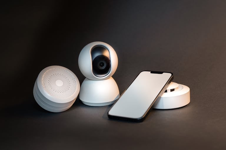 A sleek smartphone with modern smart home devices on a minimalist gray background.