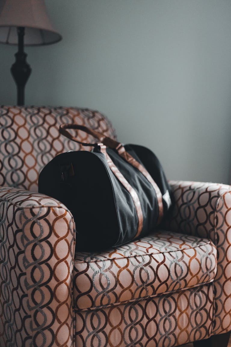 A stylish travel bag resting on a patterned armchair in a cozy indoor setting.