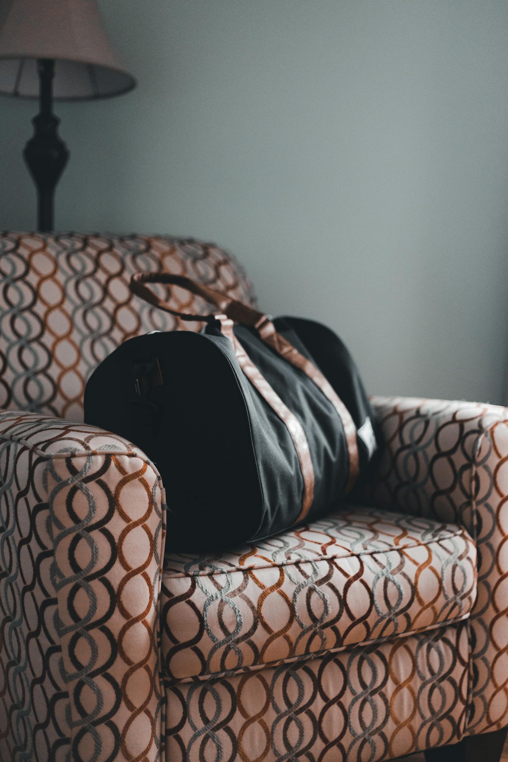 A stylish travel bag resting on a patterned armchair in a cozy indoor setting.