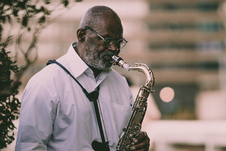 An elderly musician playing a saxophone outdoors in a serene setting.