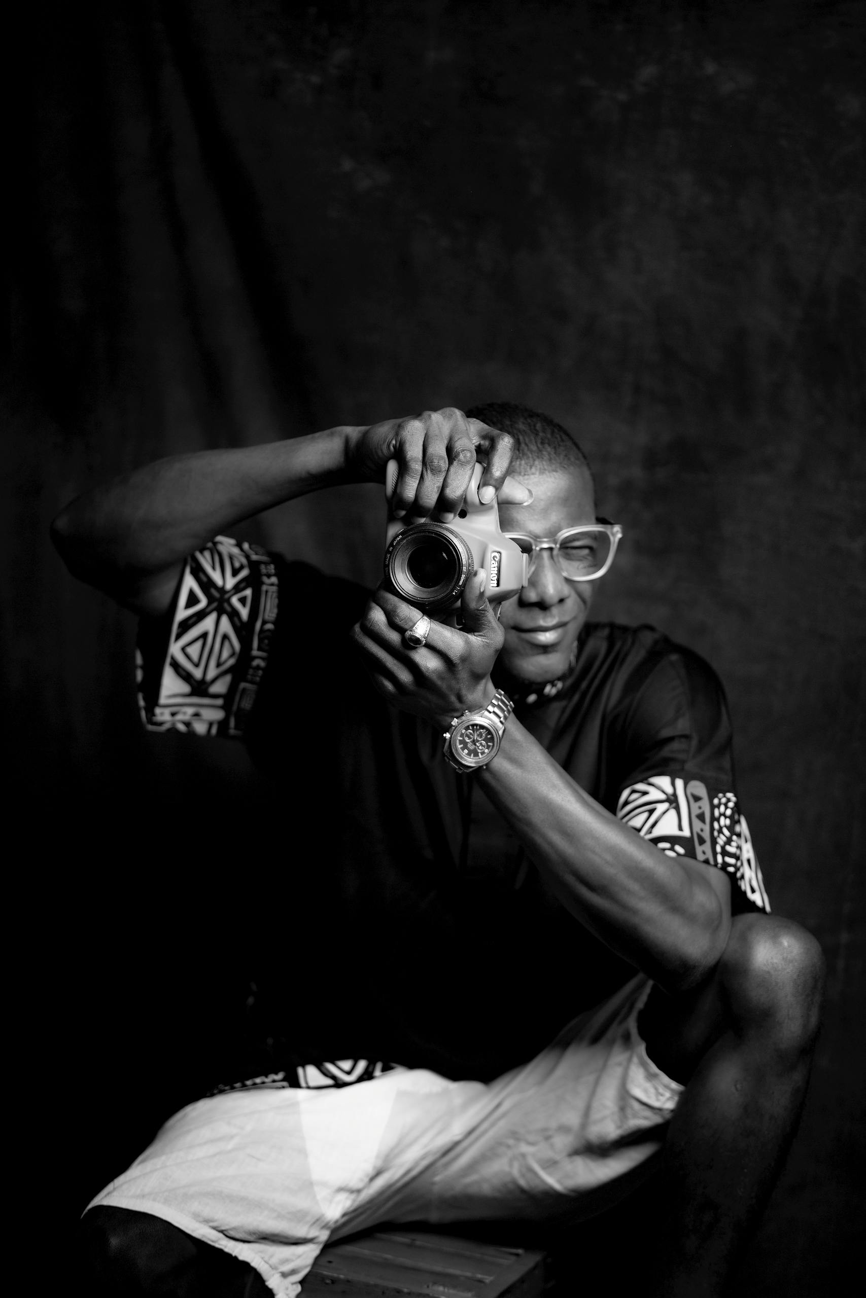 Artistic black and white portrait of a man sitting and posing with a camera.