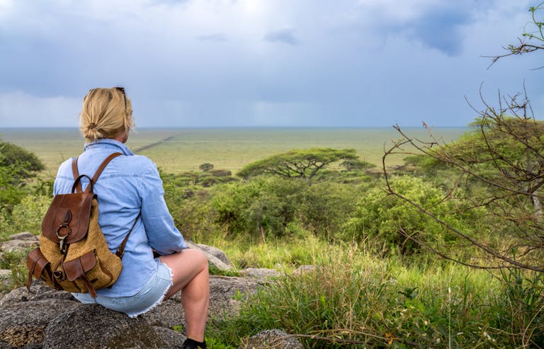 Blonde woman with backpack enjoying view of expansive African landscape under overcast skies.