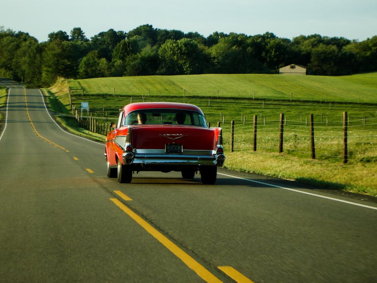 Classic red car driving on a scenic countryside road in Ohio, capturing a vintage travel vibe.