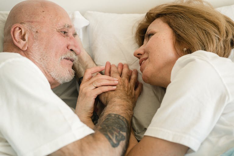 Close-up of a senior couple holding hands and smiling at each other while lying in bed, showcasing love and connection.