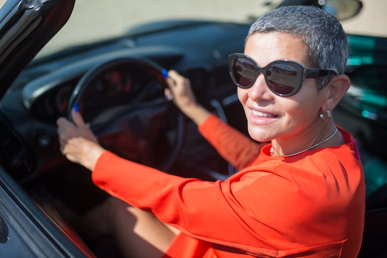 Confident woman in a convertible wearing sunglasses, enjoying a drive under the sun.