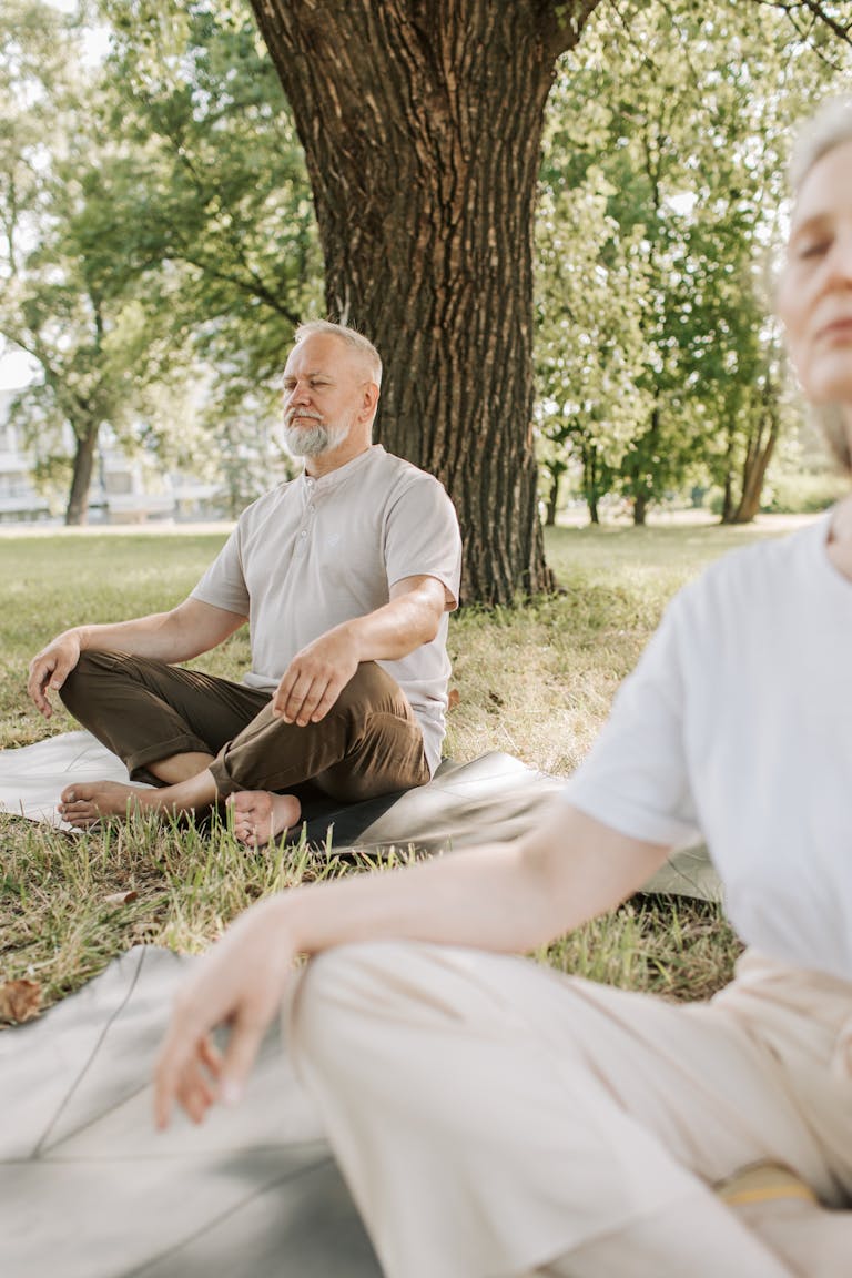 Elderly couple meditating outdoors in a serene park setting for a healthy lifestyle.