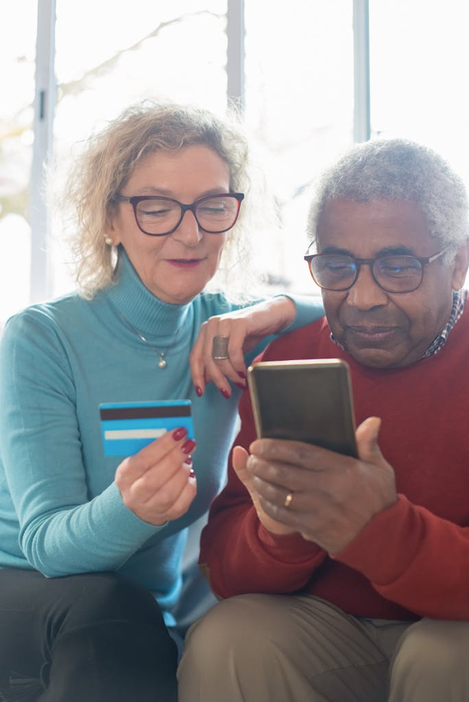 Elderly couple using smartphone and credit card for online shopping indoors.