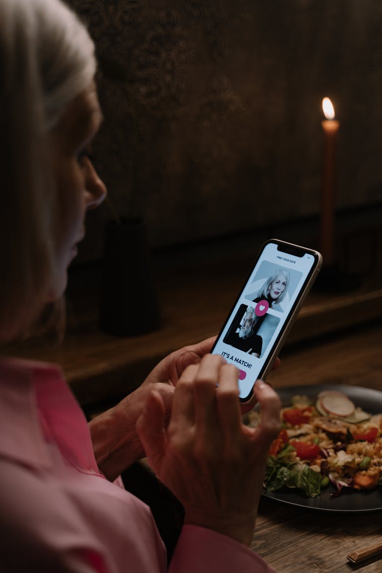 Elderly woman explores dating app during a cozy dinner.