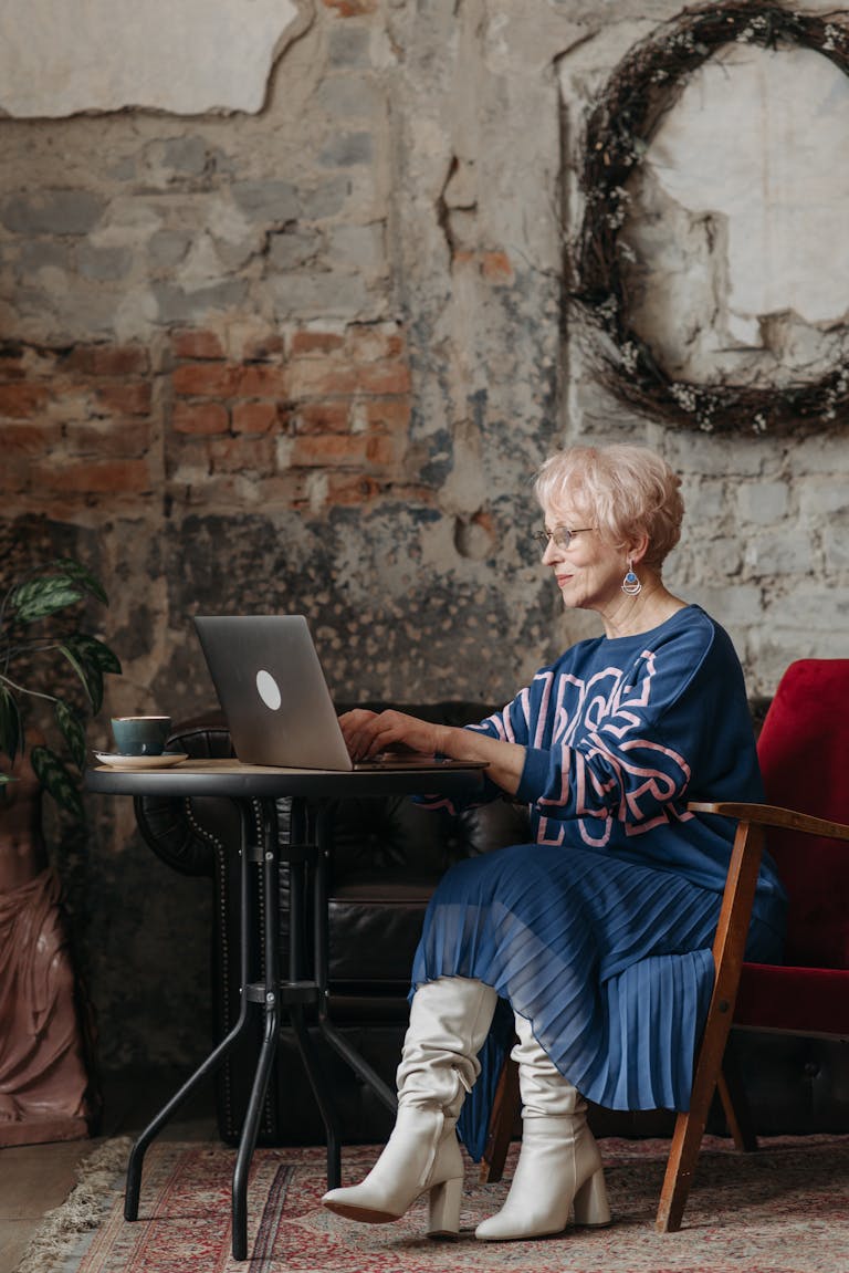 Elderly woman in a stylish outfit working on a laptop in a cozy indoor setting.