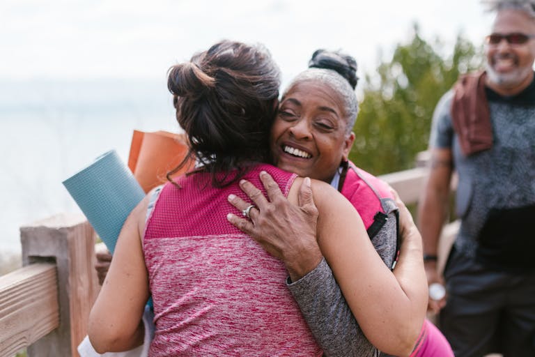 Friends embracing joyfully outdoors with yoga mats, radiating happiness and connection.