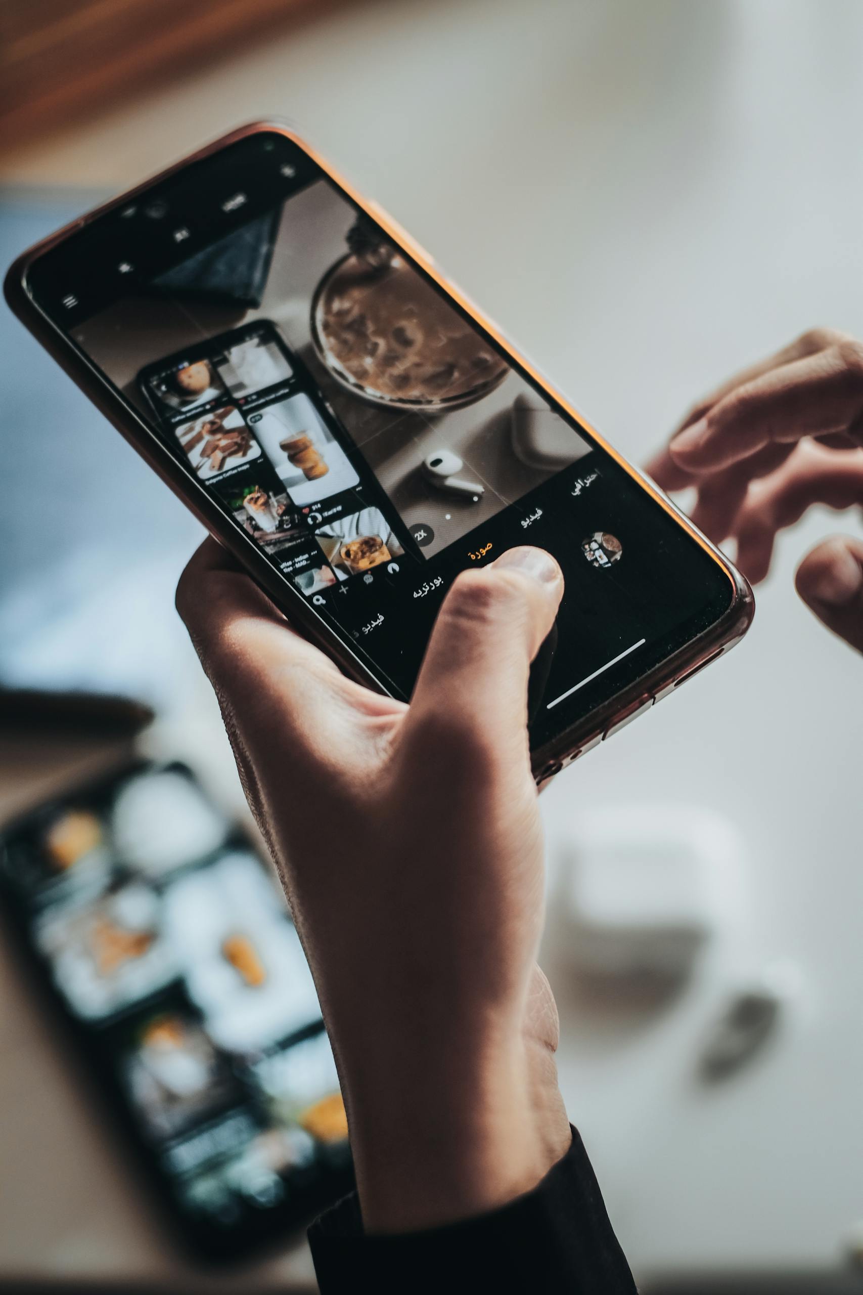 Hands using smartphone to capture a tabletop scene in Tadjenanet, Algeria.