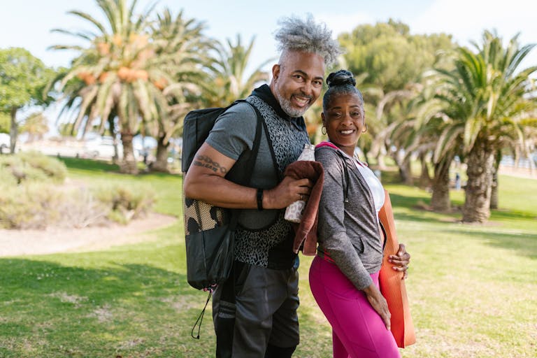 Happy senior couple practicing yoga outdoors in a park setting, promoting wellness and togetherness.