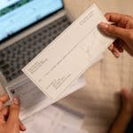 Individual holding a cheque over laptop, signifying online banking or financial transaction.