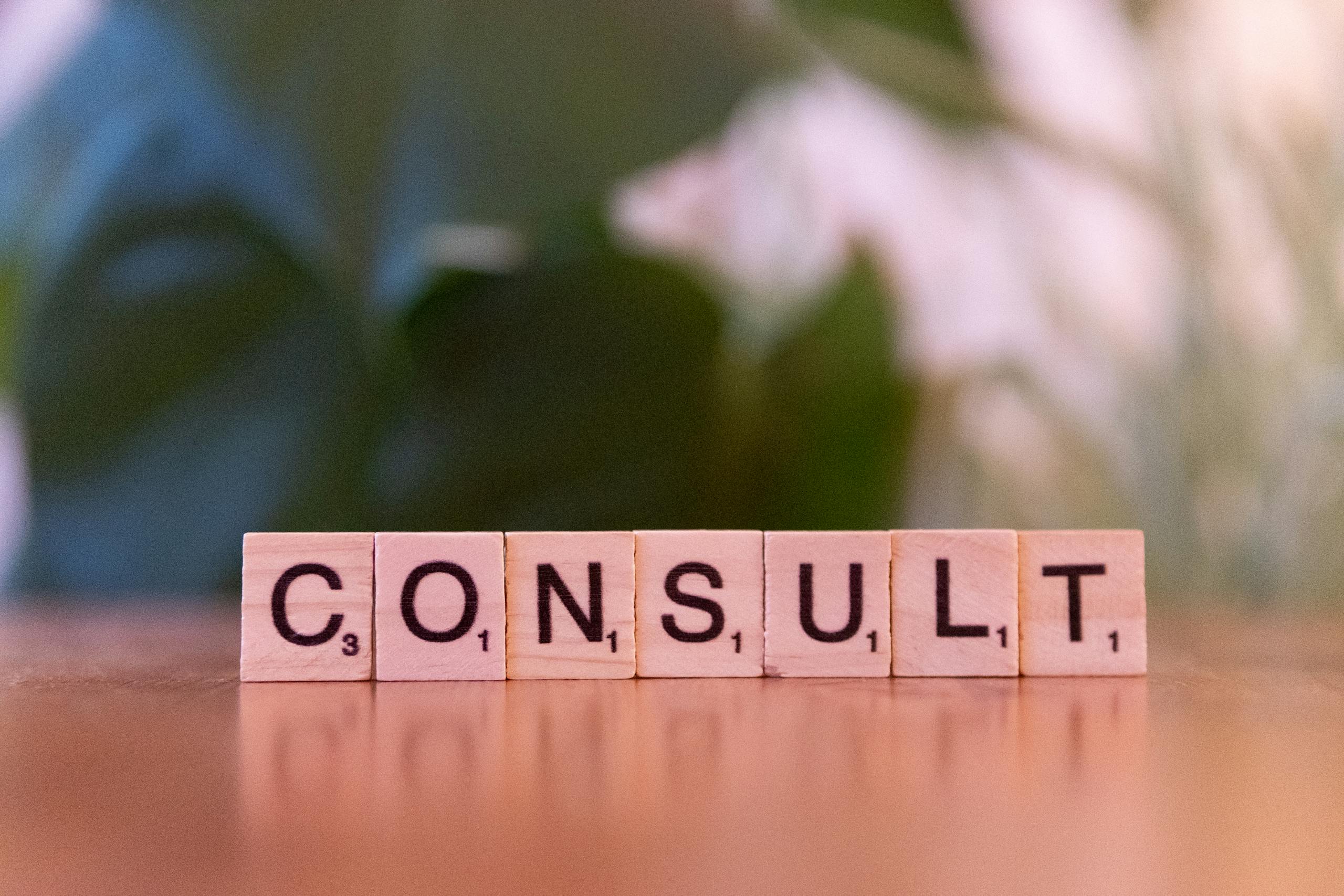 Scrabble tiles spelling 'CONSULT' on a wooden table with blurred background.