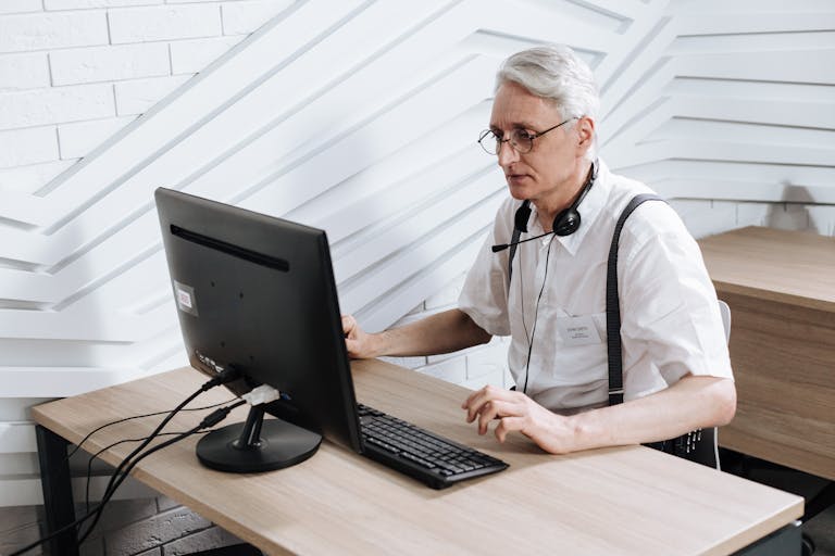 Senior adult man working in a call center with a headset and computer.