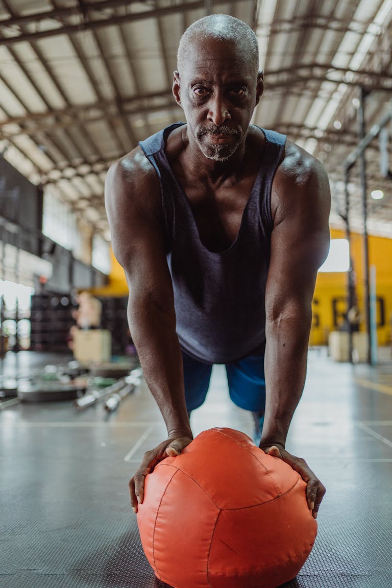 Senior adult performing push up exercise with medicine ball in gym setting.
