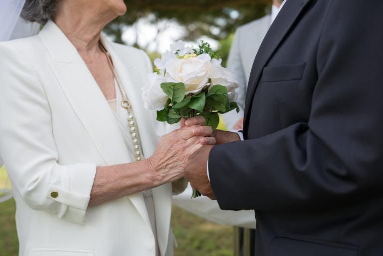 Senior couple exchanging vows and holding hands at an outdoor wedding ceremony.