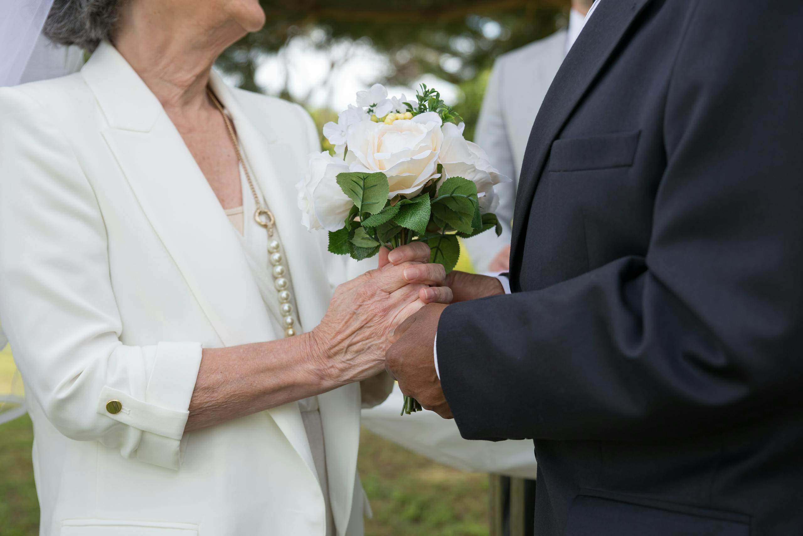 Senior couple exchanging vows and holding hands at an outdoor wedding ceremony.
