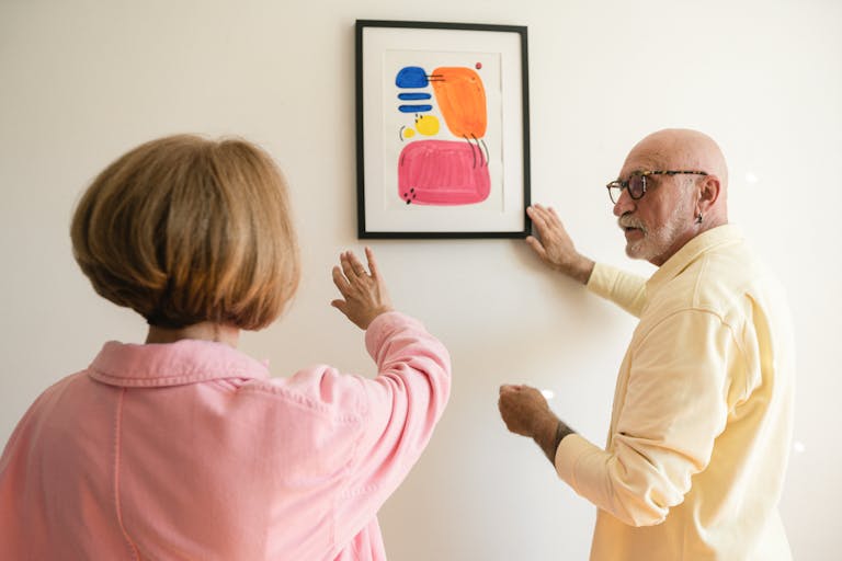 Senior couple hanging colorful modern artwork, showcasing their artistic taste.