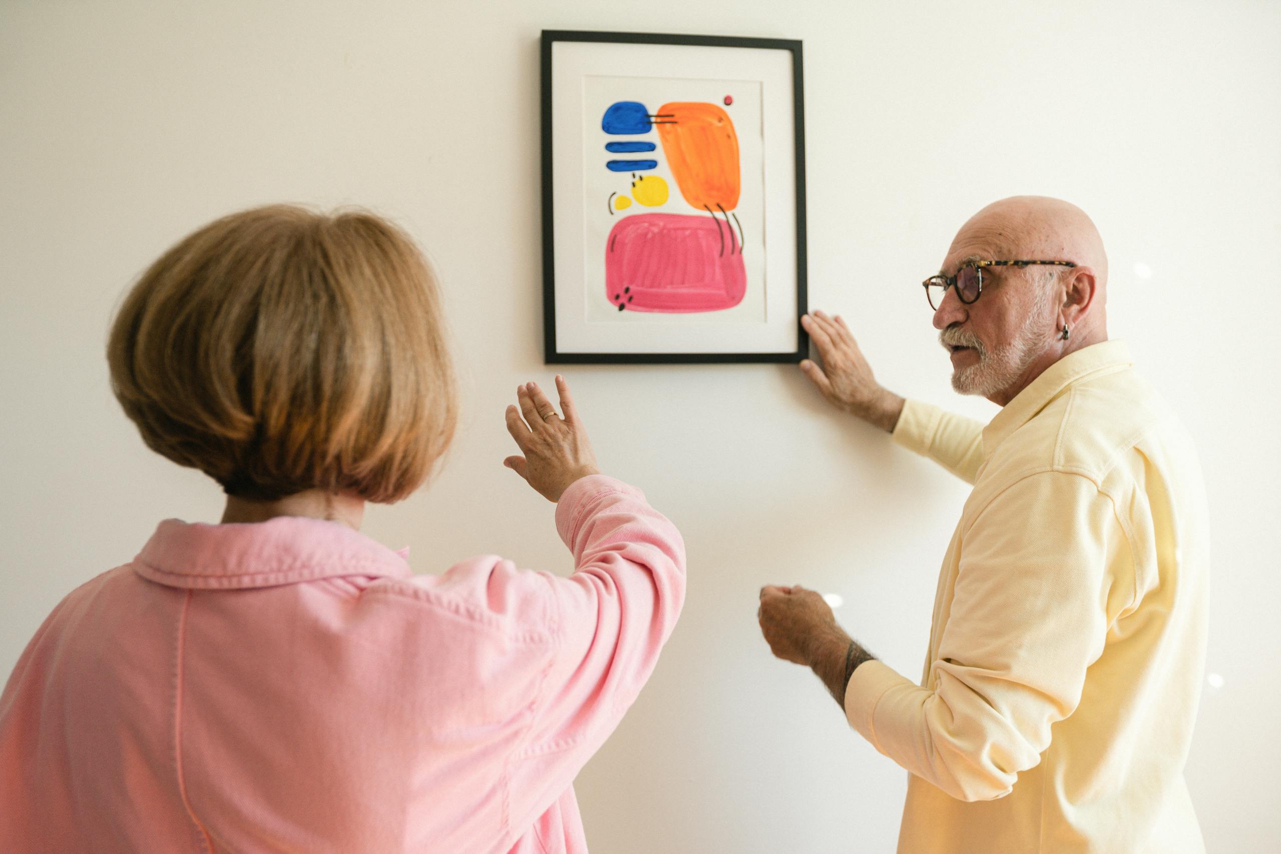 Senior couple hanging colorful modern artwork, showcasing their artistic taste.