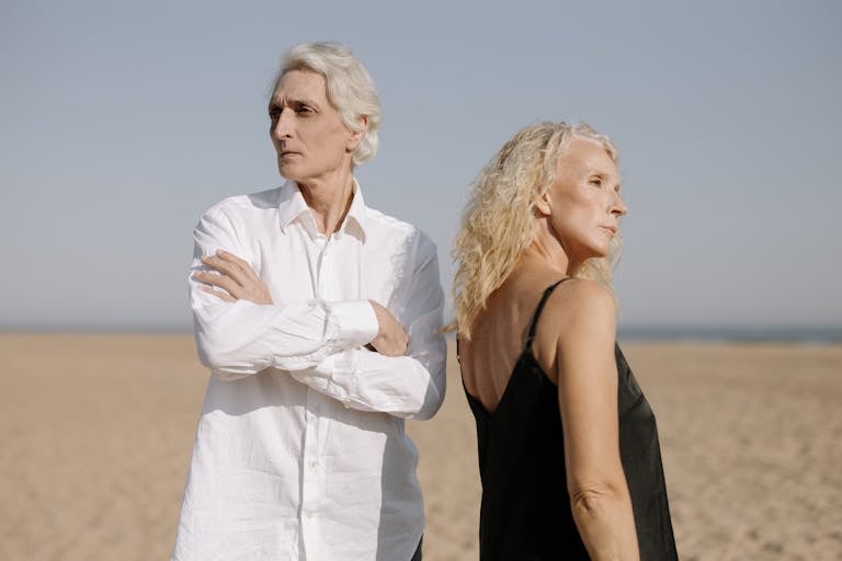 Senior couple poses on a sunlit beach, showcasing elegance and style in a serene setting.
