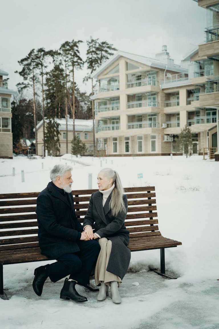 Senior couple sitting on a bench in a snowy urban setting, sharing affectionate moments.