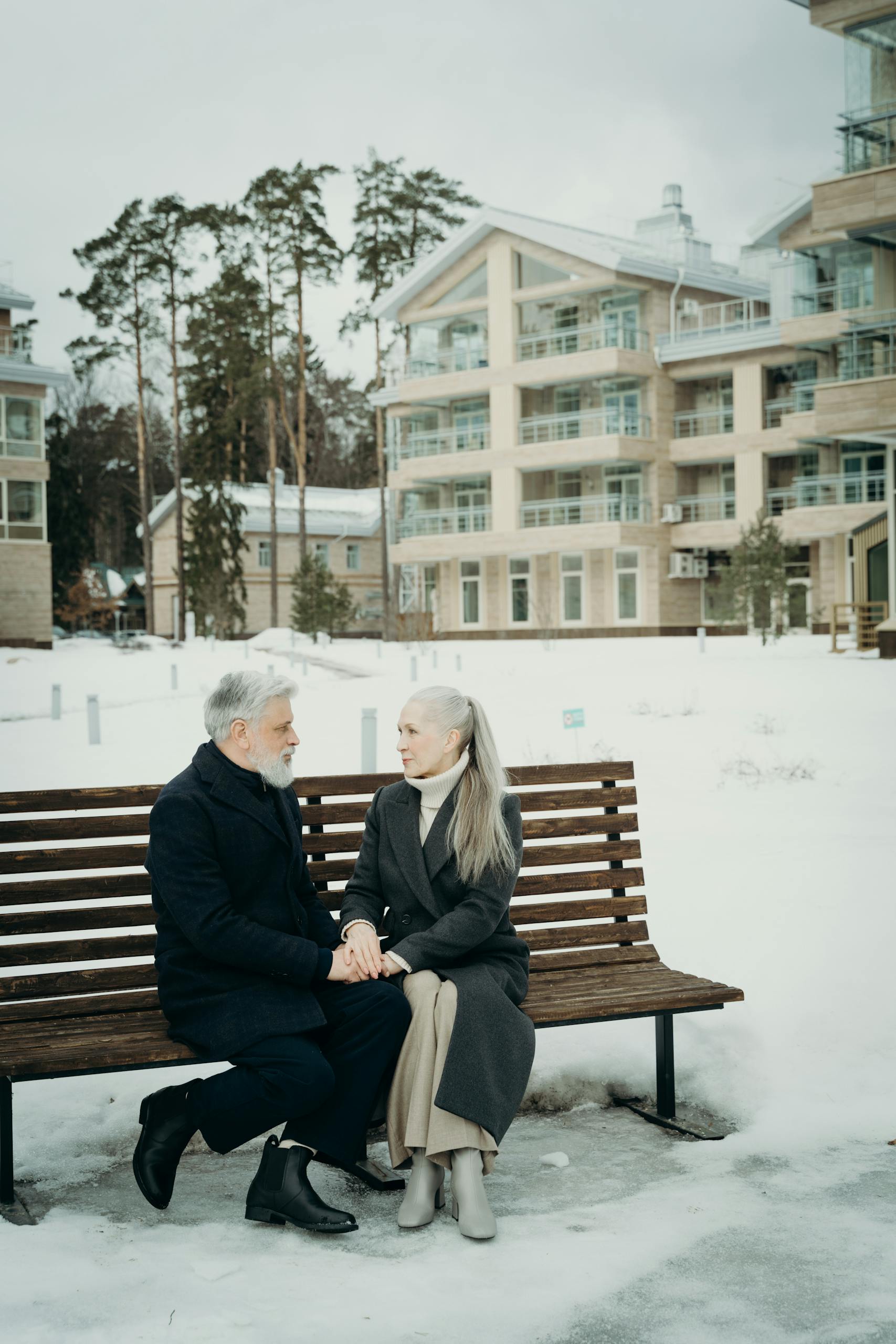 Senior couple sitting on a bench in a snowy urban setting, sharing affectionate moments.