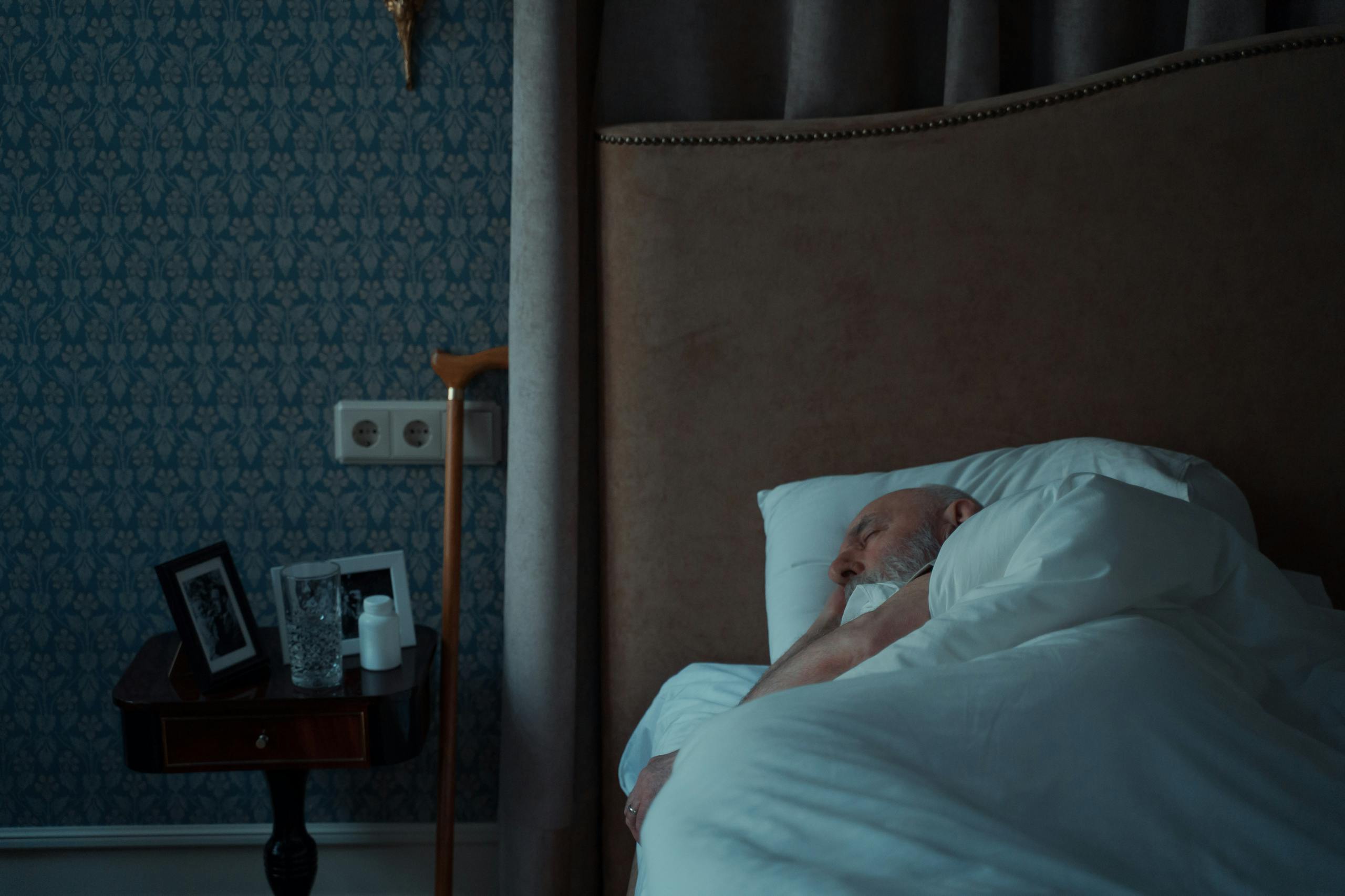Senior man sleeping in a stylish bedroom with a nightstand and framed photos.