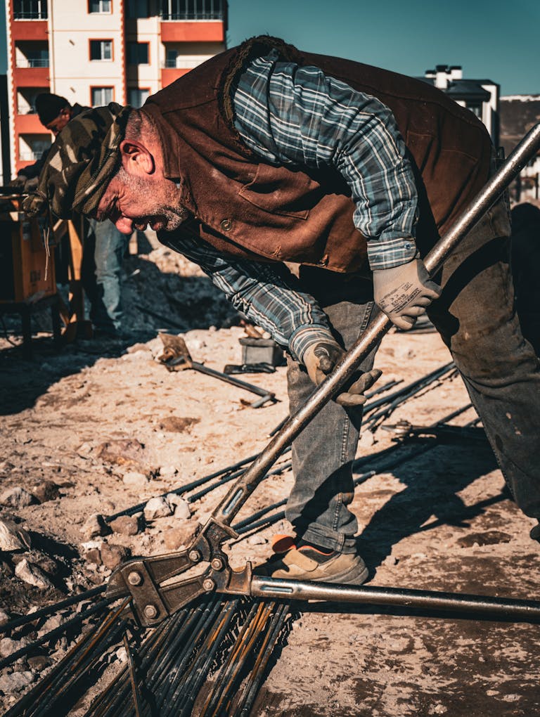 Senior man working on construction site in Türkiye, bending metal rods under sunny sky.