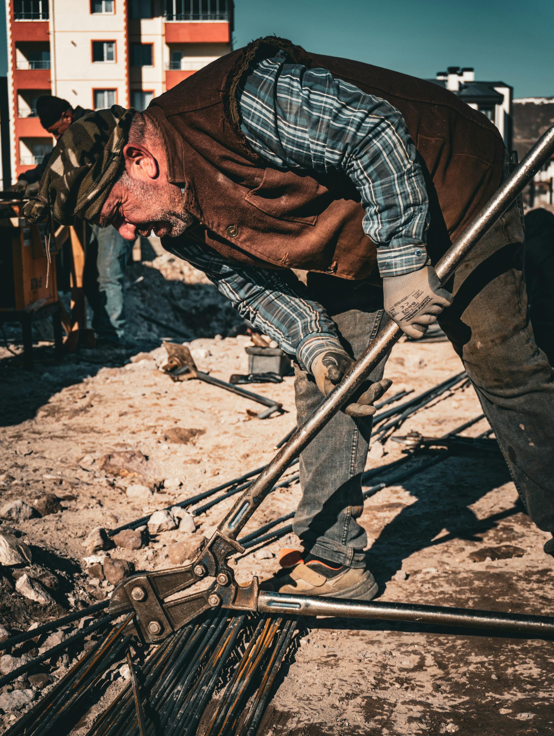 Senior man working on construction site in Türkiye, bending metal rods under sunny sky.