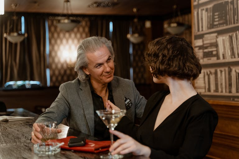 Two adults enjoying drinks and conversation in a stylish bar, surrounded by cozy decor.