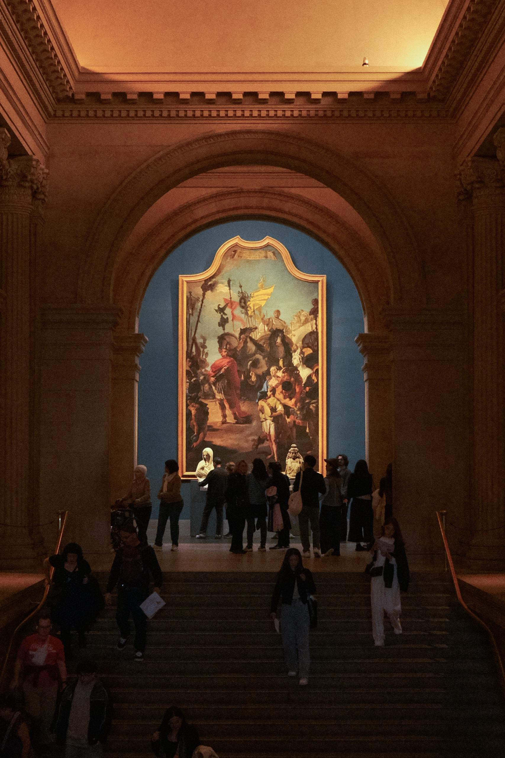 Visitors admire artwork under a grand archway at a New York City museum.
