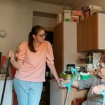 A caregiver engaging with a senior using crutches in a cozy Prague home environment.
