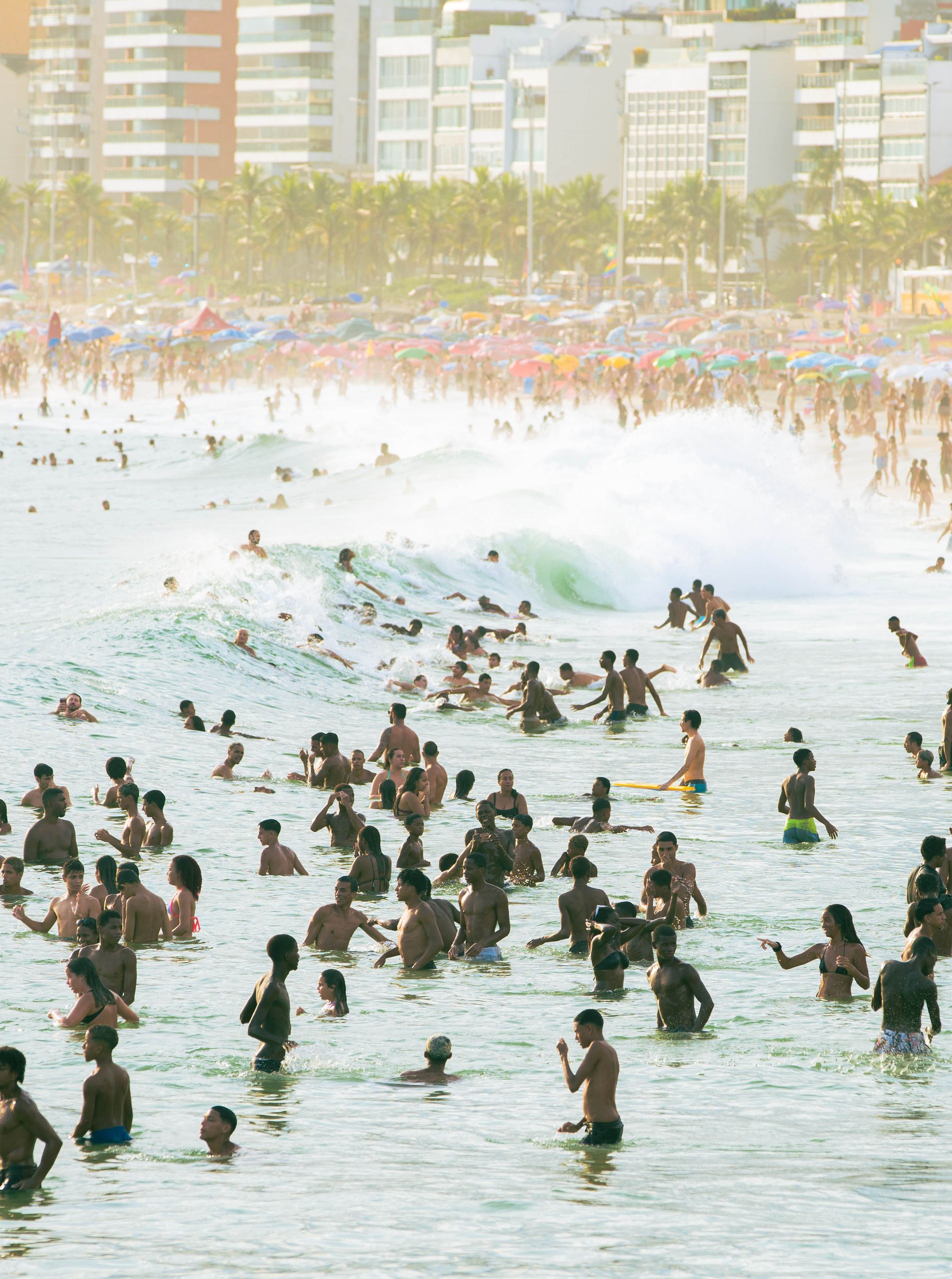A lively beach scene with numerous people enjoying the ocean waves and sunny weather.