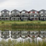A row of modern houses reflected in a calm pond, showcasing serene suburban architecture.