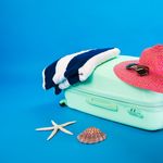 Beach essentials including a suitcase, hat, towel, and seashells on a bright background.