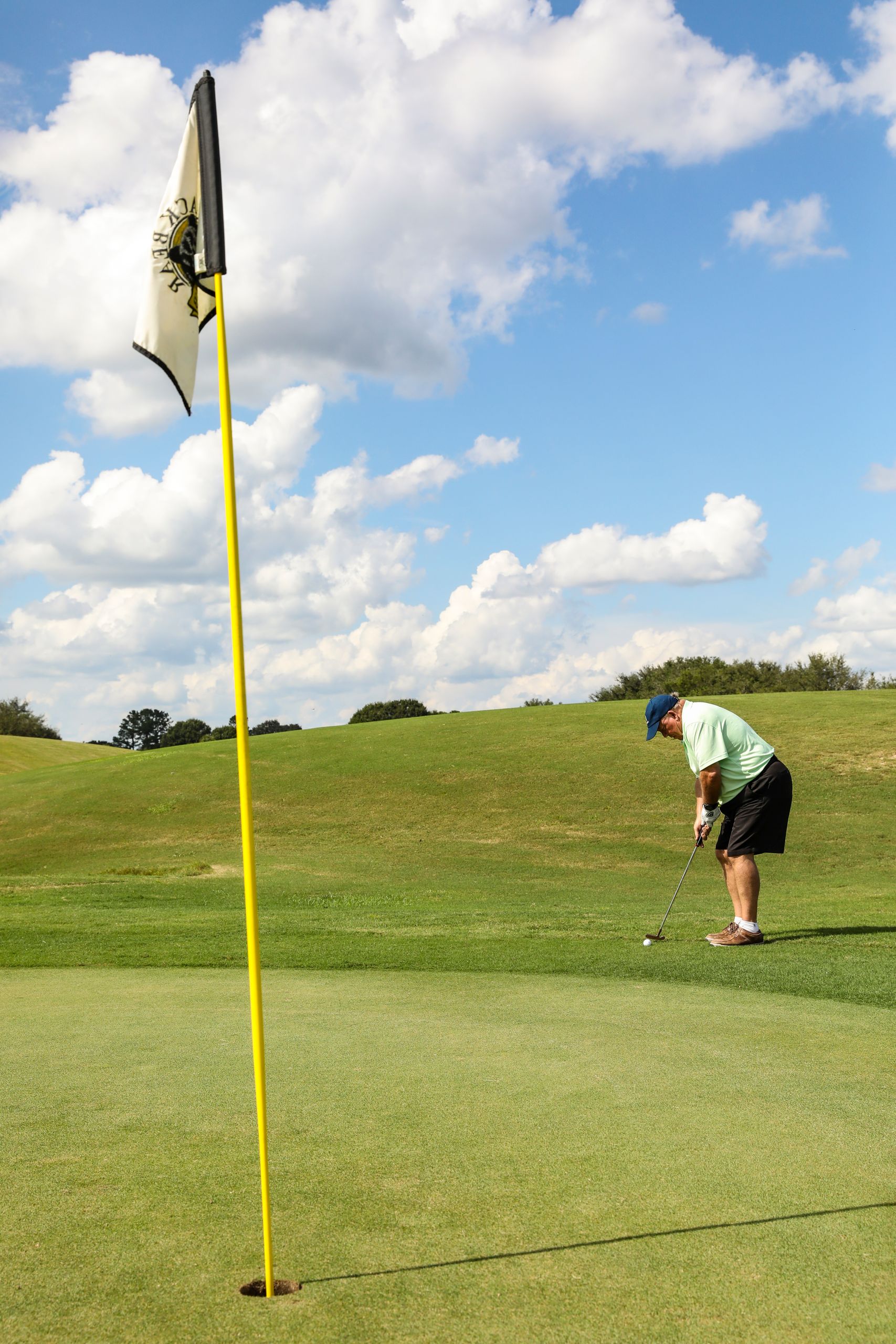 Elderly man golfing on a sunny day at Eustis golf course, captured during a putt.