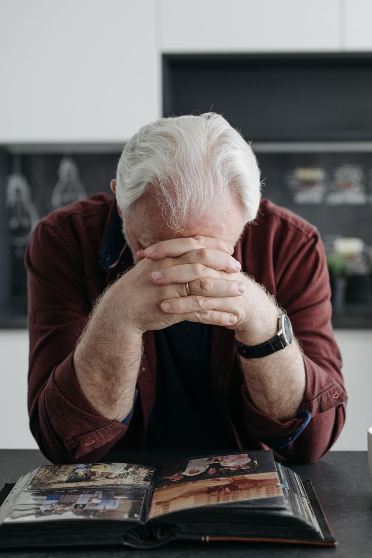 Elderly man with white hair contemplating past memories through a photo album at home.