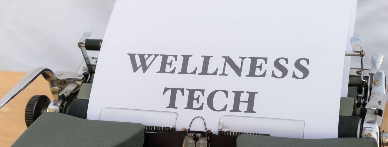 A close-up of a vintage typewriter featuring a paper with the words 'Wellness Tech.'